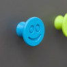 Flexible furniture knob with smile, blue, on dark background.