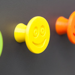 Flexible furniture knob with smile, yellow, on dark background.