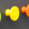 Flexible furniture knob with smile, yellow, on dark background.