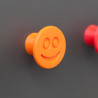 Flexible furniture knob with smile, orange, on dark background.