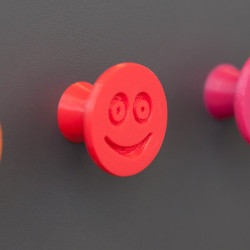 Flexible furniture knob with smile, red, on dark background.