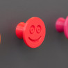 Flexible furniture knob with smile, red, on dark background.