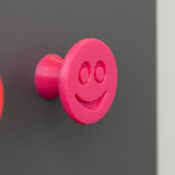 Flexible furniture knob with smile, pink, on dark background.