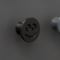 Flexible furniture knob with smile, black, on dark background.