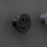 Flexible furniture knob with smile, black, on dark background.