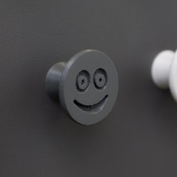 Flexible furniture knob with smile, graphite, on dark background.
