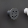 Flexible furniture knob with smile, graphite, on dark background.