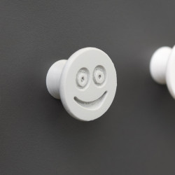 Flexible furniture knob with smile, grey, on dark background.