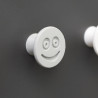 Flexible furniture knob with smile, grey, on dark background.