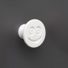 Flexible furniture knob with smile, white, on dark background.