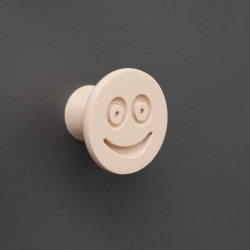 Flexible furniture knob with smile, beige, on dark background.