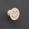 Flexible furniture knob with smile, beige, on dark background.